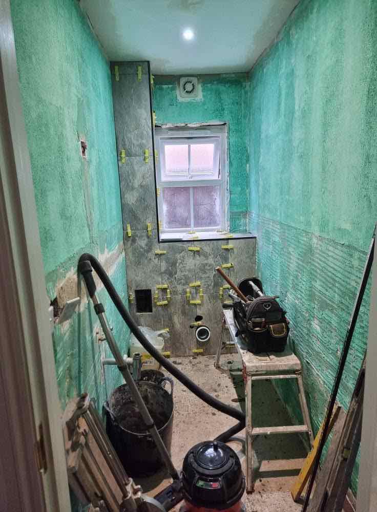 Bathroom mid-renovation with waterproof tanking and tiling underway around a window