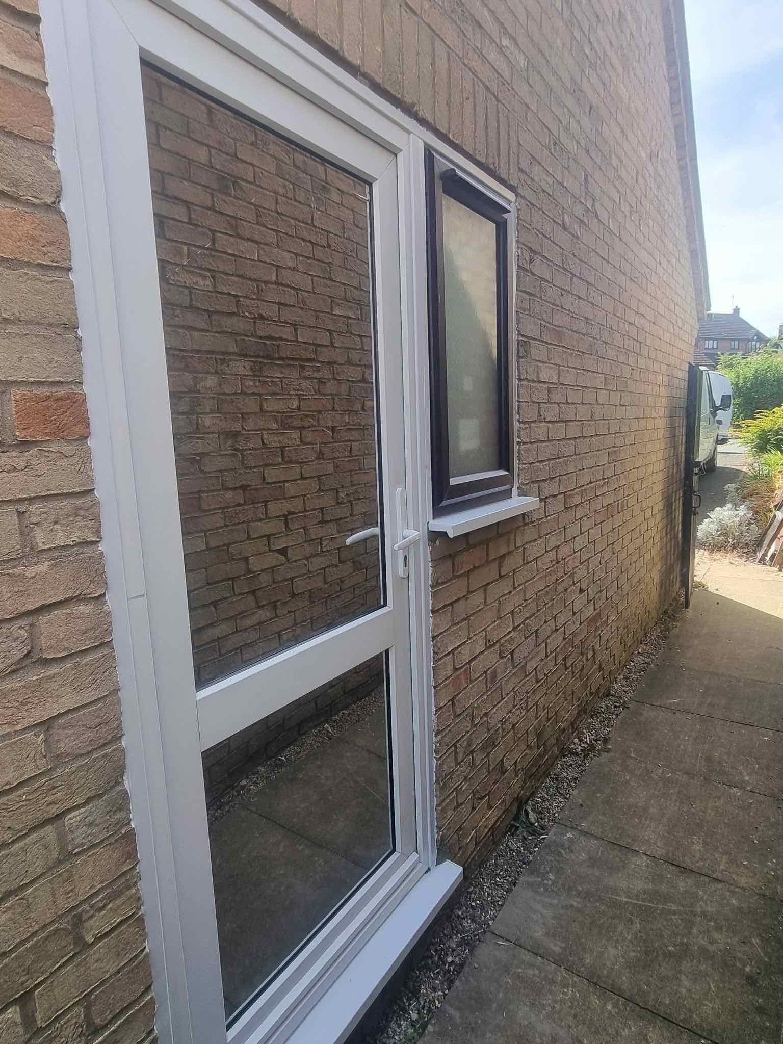 New white uPVC side door and window fitted into a brick house wall