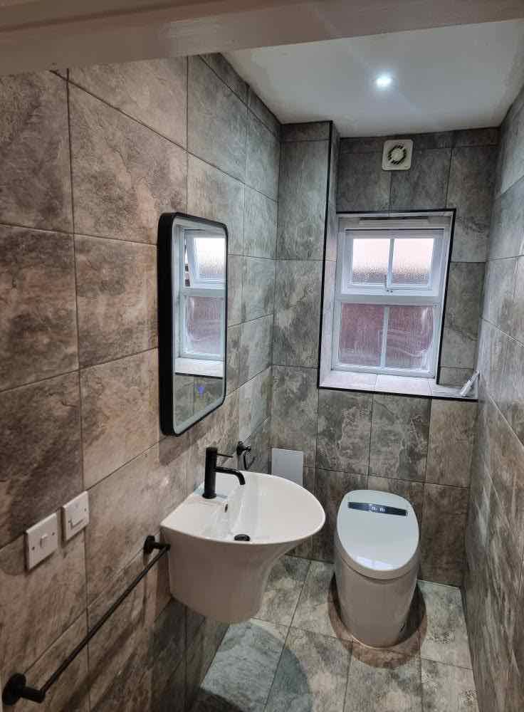 Finished cloakroom with dark stone-effect tiling, wall-hung basin and black tapware