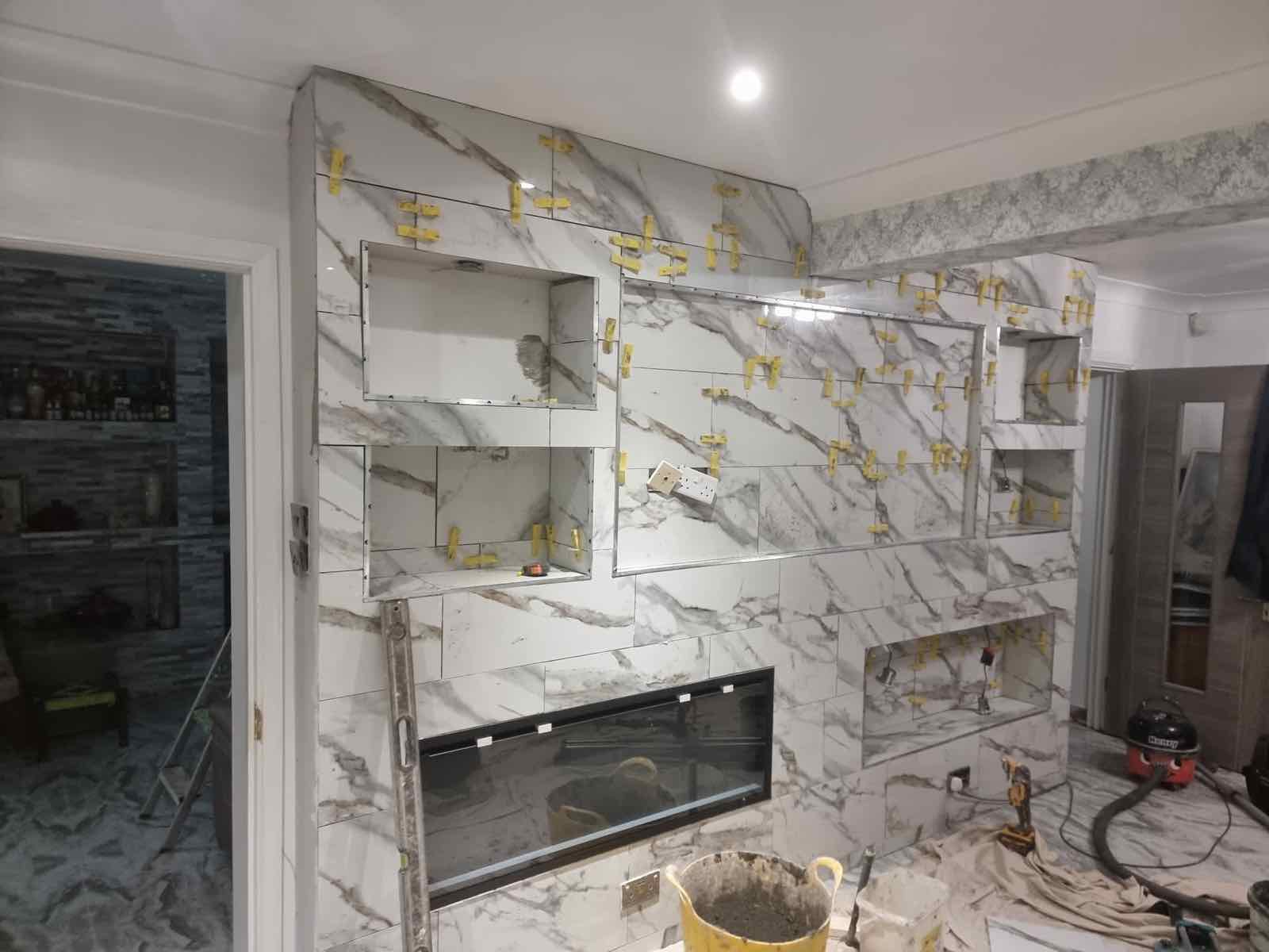 Large-format marble-effect porcelain tiling in progress around a fireplace and alcove shelving