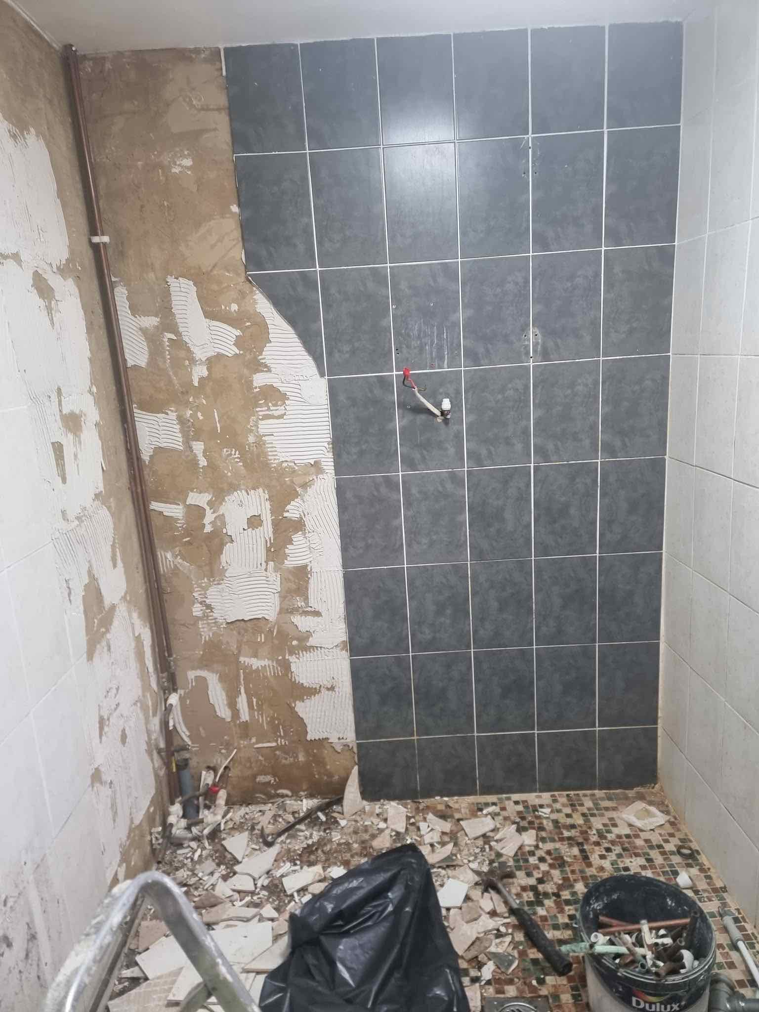 Old bathroom tiles stripped back with new dark tiling going up over exposed pipework